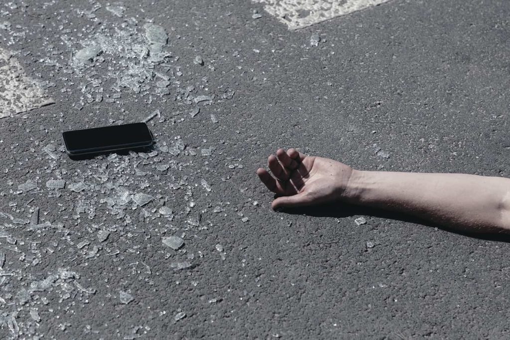 mans disembodied arm with a cell phone on the pavement