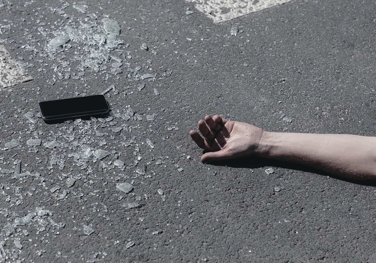 mans disembodied arm with a cell phone on the pavement