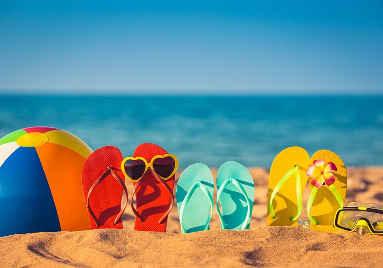 flip flops with sunglasses and a beach ball on the sand